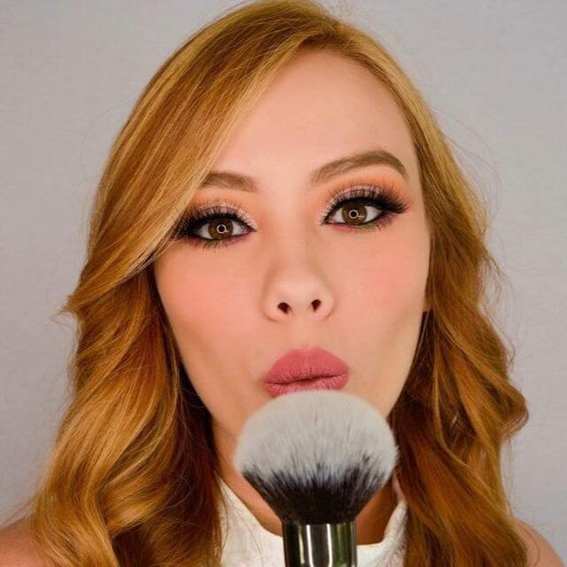 Maquilladora profesional con brocha enseñando un look soft glam impecable.